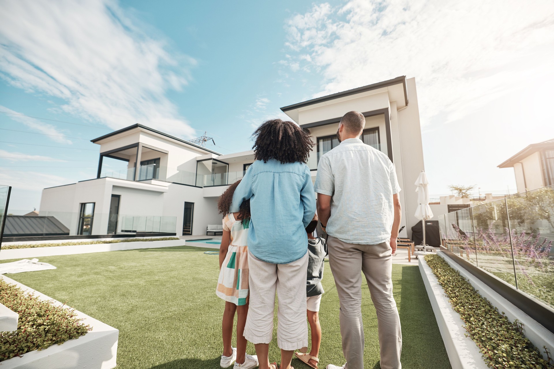 Love, new house and family in their backyard together looking at their property or luxury real estate. Embrace, mortgage and parents with their children on grass at their home or mansion in Canada.