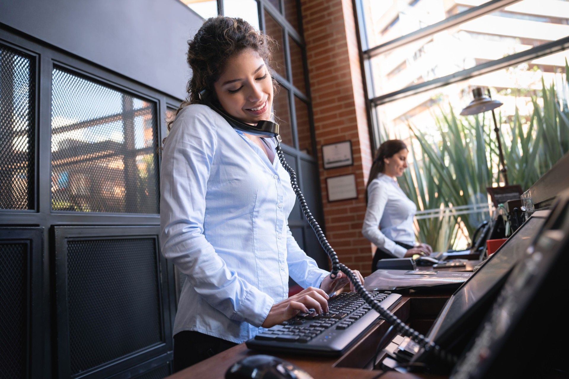 Beautiful hotel receptionist on a phone call looking at the bookings on system smiling